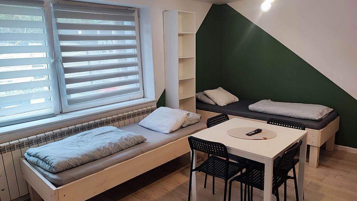 Sypialnia 1: łóżka, stół i zielona ściana z oknem